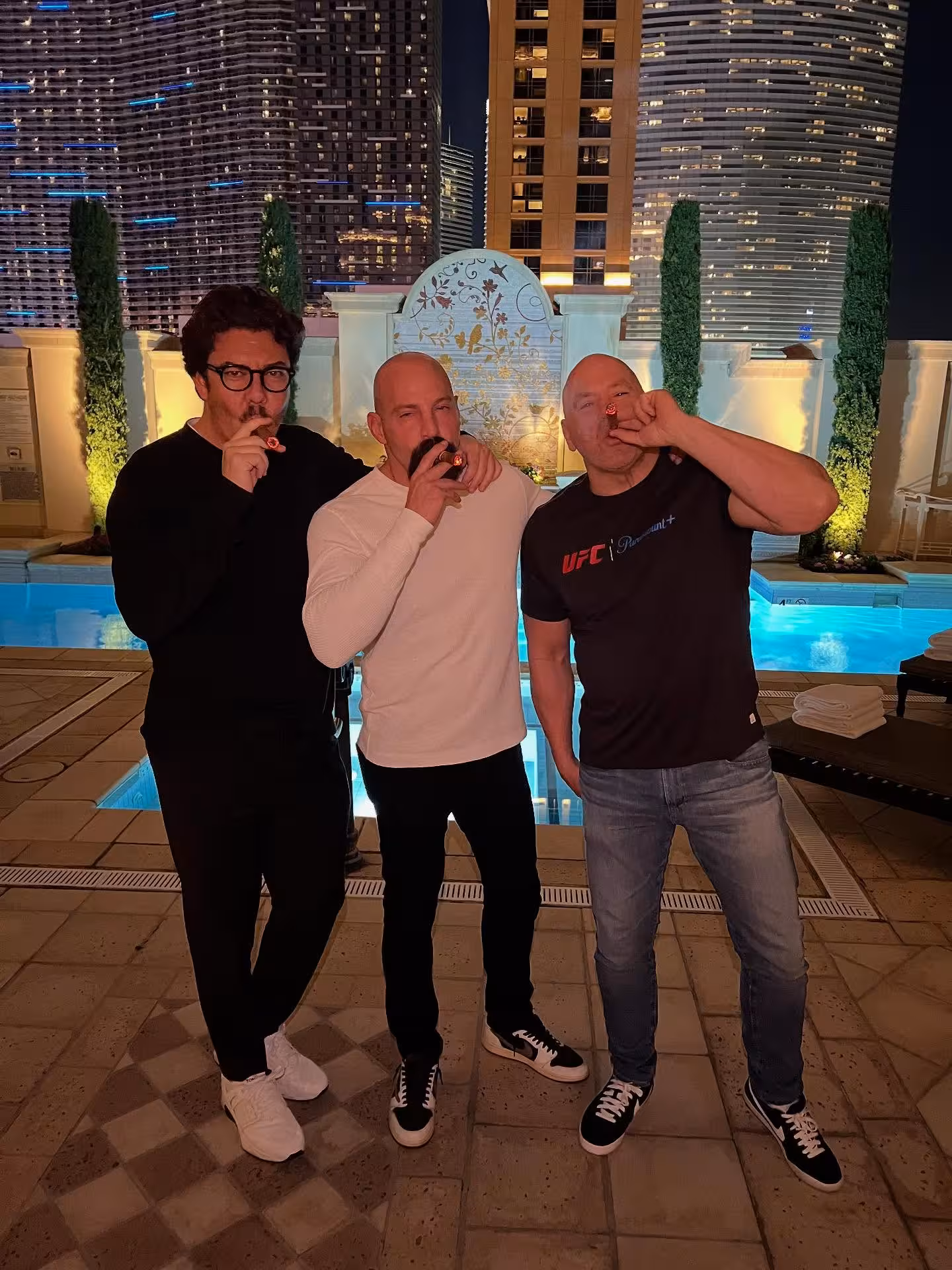 smoking cigars by a rooftop pool at night with luxury high rise buildings in the background during a UFC related event